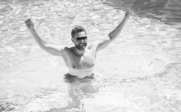 Feliz homem barbudo em óculos de sol se divertindo na água da piscina nas férias de verão férias de verão