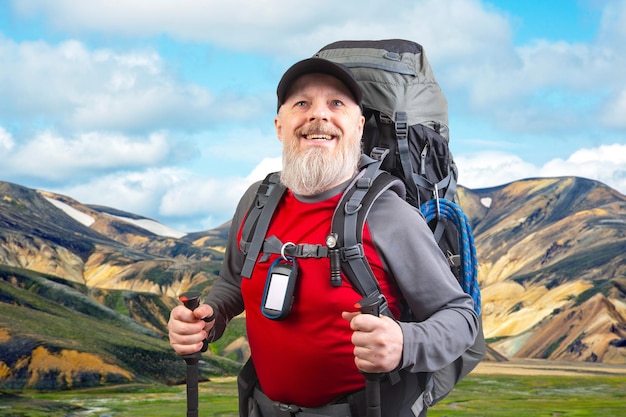 feliz homem barbudo viajante com equipamentos de caminhada contra o pano de fundo de uma montanha