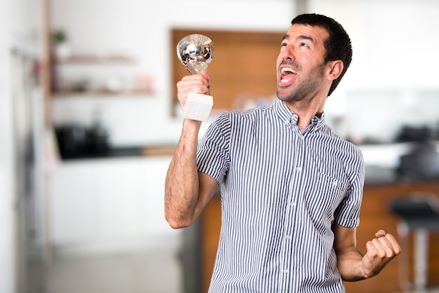 Foto feliz, homem bonito, segurando um troféu dentro da casa