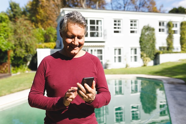 Feliz homem caucasiano sênior usando smartphone no jardim ensolarado. estilo de vida de aposentadoria de luxo, passando o tempo em casa.