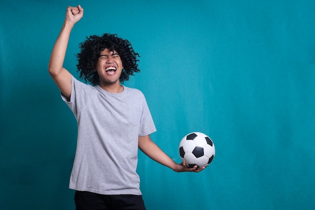 Feliz homem encaracolado fã de futebol gritando apoio time favorito segura bola de futebol fazendo gesto de vencedor