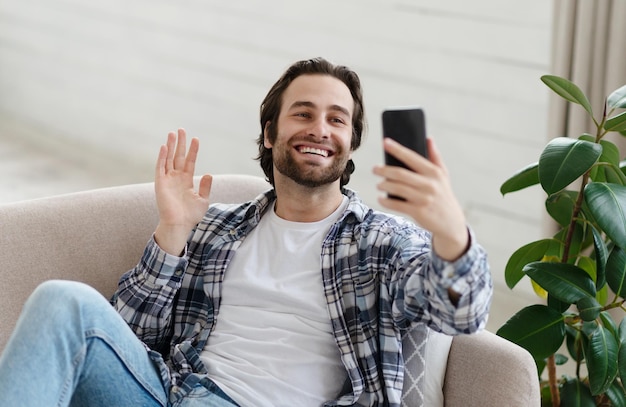 Feliz homem europeu milenar com restolho em conversas casuais por vídeo on-line acenando com a mão para a câmera