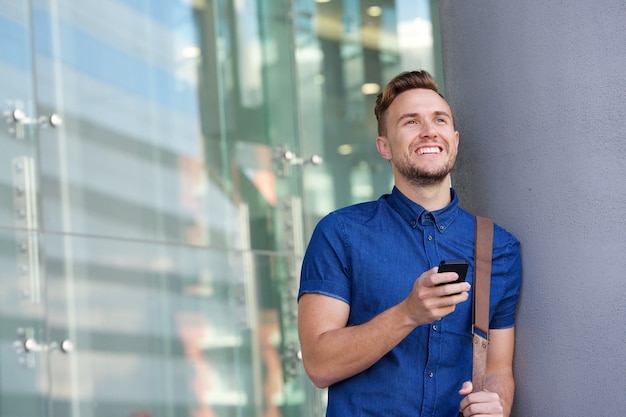 Feliz, homem jovem, apoiando parede, exterior, com, telefone pilha