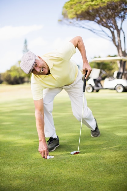 Feliz homem maduro, segurando o taco de golfe enquanto dobra no campo gramado