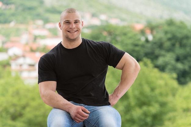 Feliz homem musculoso em camiseta preta em pé e mostrando seu músculo