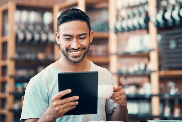 Feliz homem relaxado e despreocupado lendo notícias de mídia social em um tablet enquanto desfruta de café Jovem casual respondendo a e-mails navegando na internet ou assinando um aplicativo de namoro online em um café