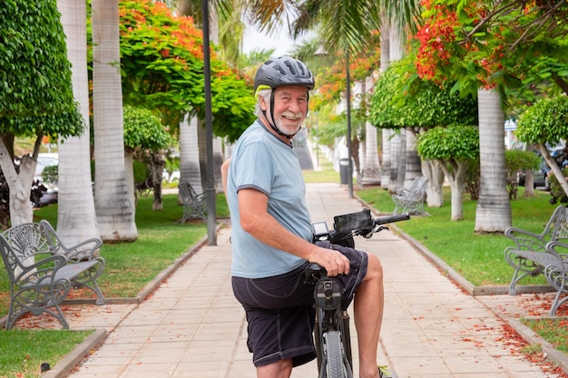 Feliz homem sênior ativo andando no parque público com bicicleta elétrica olhando para trás Conceito de estilo de vida saudável e mobilidade sustentável