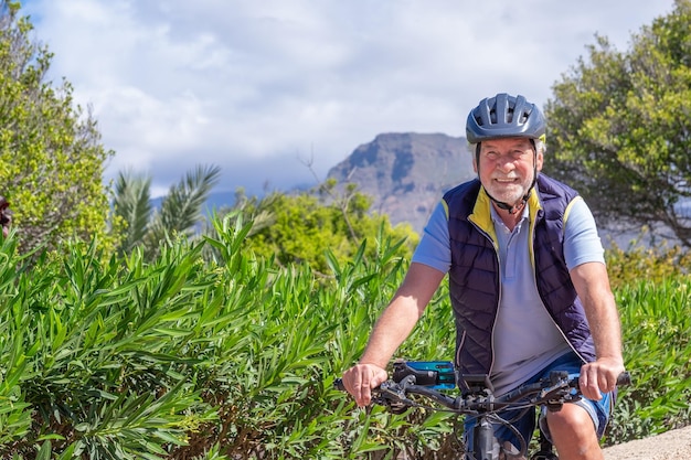 Feliz homem sênior ativo com bicicleta elétrica correndo ao ar livre no parque usando capacete e óculos de sol desfrutando de um estilo de vida saudável