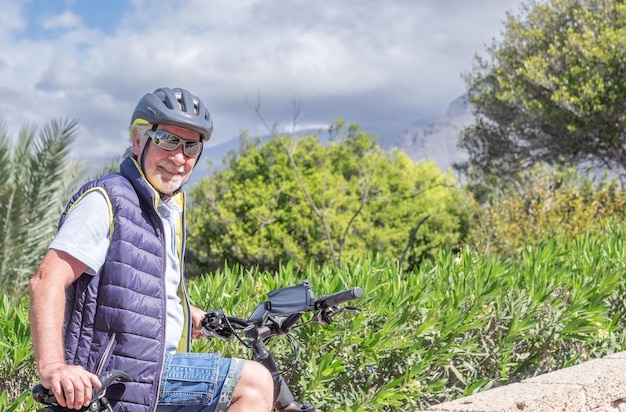 Feliz homem sênior ativo com bicicletas elétricas ao ar livre no parque Sorrindo avô idoso correndo na natureza com sua bicicleta desfrutando de um estilo de vida saudável