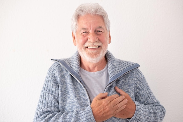 Feliz homem sênior barbudo em roupas casuais sorrindo e olhando para a câmera enquanto cruza as mãos sobre seu conceito de coração de ação de graças e amor