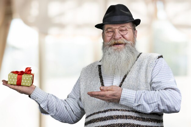 Feliz homem sênior com barba grisalha, mostrando a caixa de presente na mão.