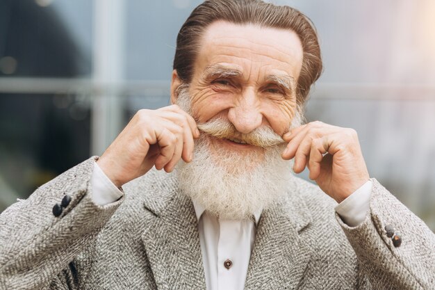 Feliz homem sênior segurando o bigode nos edifícios de escritórios