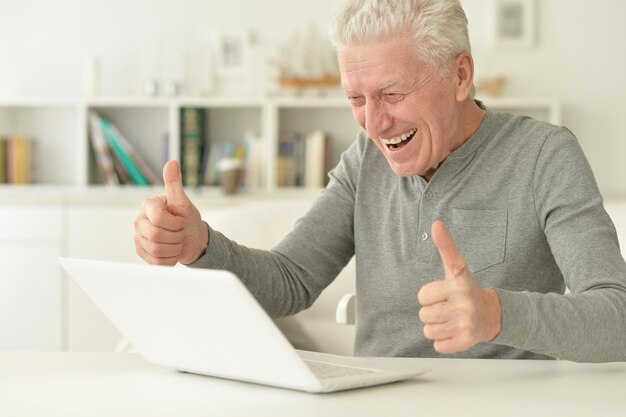 Feliz homem sênior usando laptop em casa