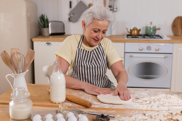 Feliz idosa cozinhando na cozinha, elegante e madura, senhora de cabelos grisalhos, avó, amassar massa