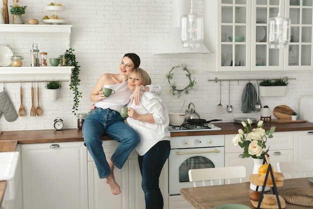 Feliz idosa mãe e filha na cozinha, bebem chá e desfrutam de uma conversa. Mãe idosa com uma filha adulta em casa