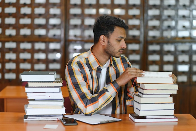 Feliz, inteligente, indiano ou árabe, estudante universitário masculino de raça mista na biblioteca