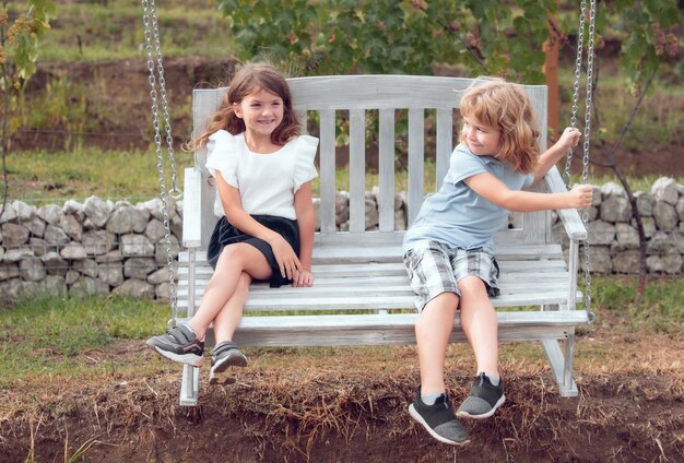 Feliz irmão e irmã balançando no balanço no parque de verão ao ar livre meninos e meninas se divertindo