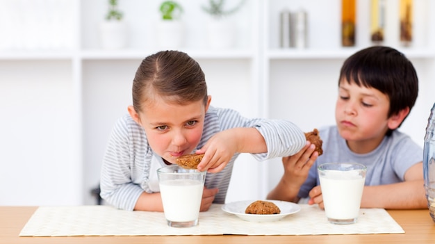 Feliz irmão e irmã comendo biscoitos e bebendo leite