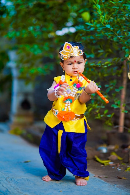 Feliz Janmashtami cartão mostrando garotinho indiano posando como Shri krishna ou kanha / kanhaiya com imagem Dahi Handi e flores coloridas.