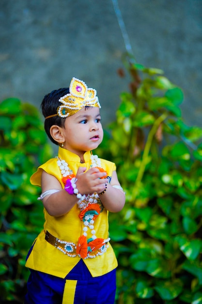 Feliz Janmashtami cartão mostrando garotinho indiano posando como Shri krishna ou kanha / kanhaiya com imagem Dahi Handi e flores coloridas.