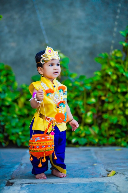 Feliz Janmashtami cartão mostrando garotinho indiano posando como Shri krishna ou kanha / kanhaiya com imagem Dahi Handi e flores coloridas.