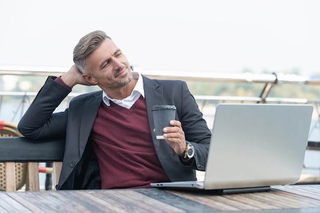 Feliz jefe descansando del trabajo durante el descanso para tomar café con una laptop en un café al aire libre