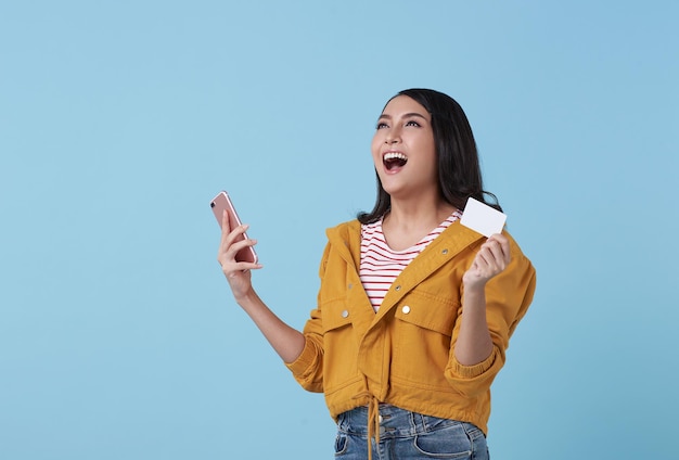 Feliz jovem adolescente asiática rindo segurando telefone celular e cartão de crédito