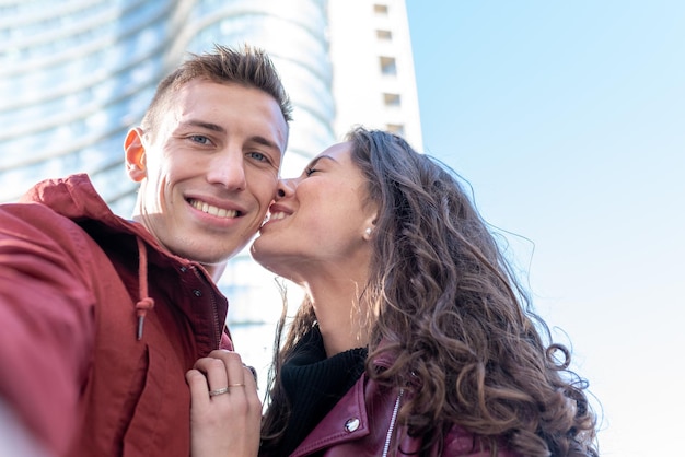 Feliz jovem adora tirar selfie quando sua namorada o beija, conceito de amor