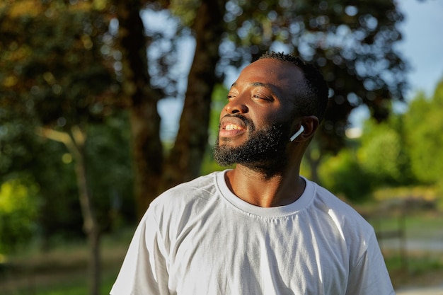 Feliz jovem adulto afro-americano andando no parque usando fones de ouvido