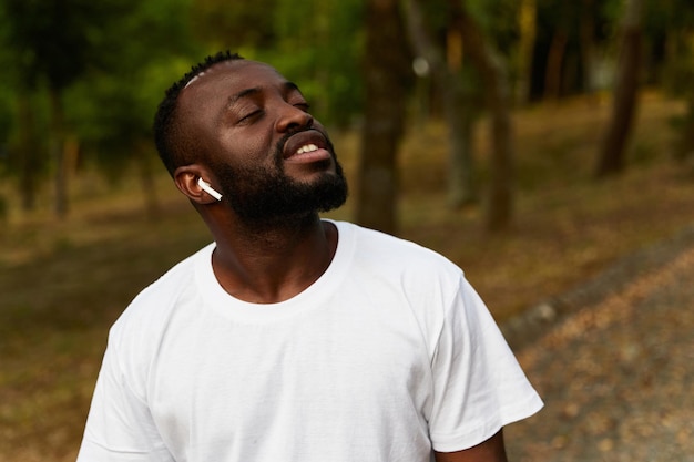 Feliz jovem adulto afro-americano andando no parque usando fones de ouvido