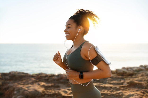 Feliz jovem afro-americana em esportes usa fones de ouvido com smartphone rodando pela manhã