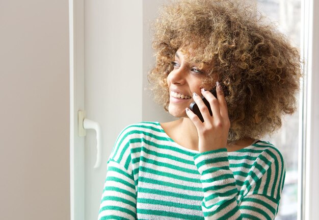 Foto feliz jovem afro-americana falando no celular pela janela