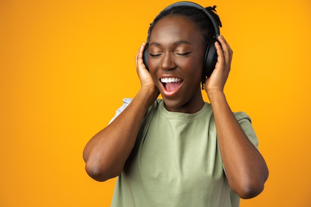 Feliz jovem afro-americana ouvindo música em fones de ouvido contra fundo amarelo