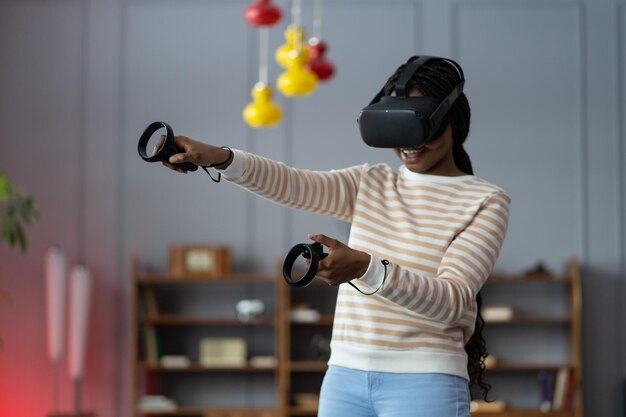 Feliz jovem afro-americana usando óculos de realidade virtual jogando videogame em casa