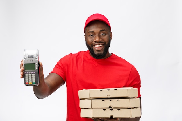 Feliz jovem afro-americano entregador segurando uma máquina de pagamento com cartão eletrônico e um produto de entrega.