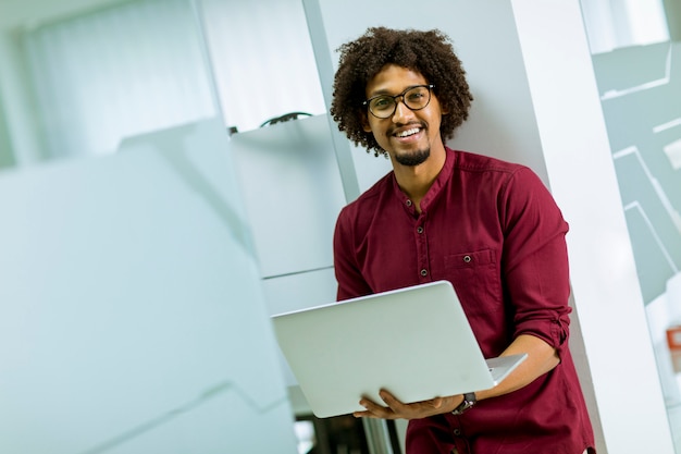 Foto feliz jovem afro-americano especialista em ti usando óculos, trabalhando em seu laptop no escritório