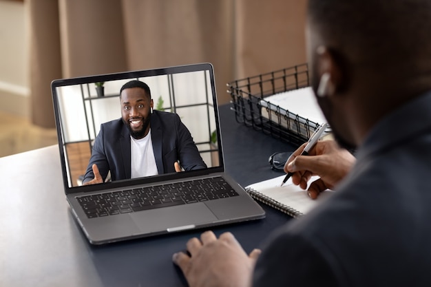 Feliz jovem afro-americano falando com seu colega de trabalho usando o laptop. Videochamada, conceito de auto-isolamento