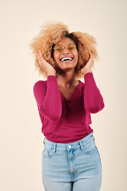 Feliz jovem afro tocando seu cabelo e sorrindo em pé sobre um fundo isolado.
