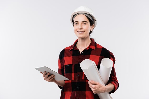 Feliz jovem arquiteta usando capacete e flanela usando o touchpad enquanto trabalhava em um novo projeto na frente da câmera, isolada