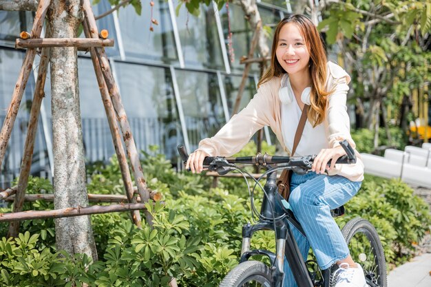 Feliz jovem asiática bonita andando de bicicleta na rua ao ar livre perto da cidade de construção, retrato de estilo de vida feminino sorridente usando bicicleta em meios de transporte de viagens de verão, ecologicamente correto