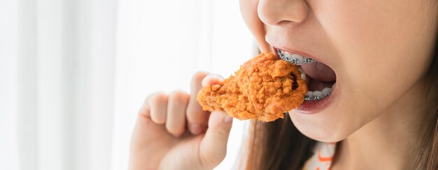 Feliz jovem asiática com aparelho segurando frango frito para comer.