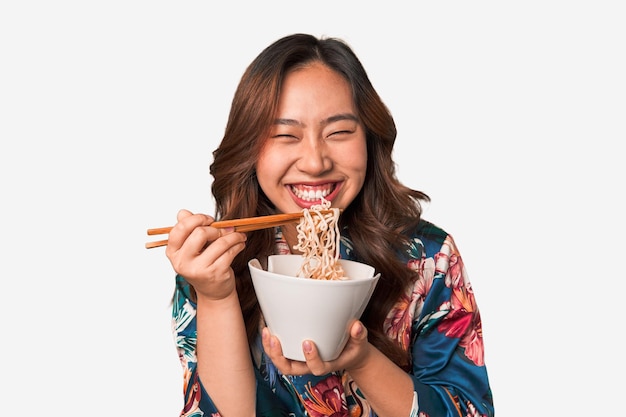 Feliz jovem asiática comendo macarrão com pauzinhos