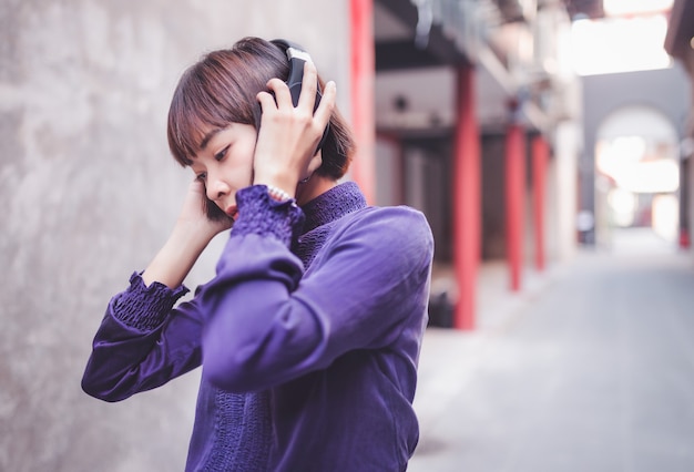 Feliz jovem asiática ouvindo música com fones de ouvido na rua.