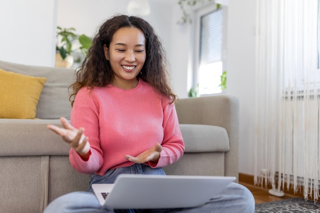 Feliz jovem asiática se divertindo fazendo videochamada usando laptop em sua casa acenando com a mão videoconferência chamando no laptop sente-se no sofá distância aprenda zoom reunião virtual online em casa