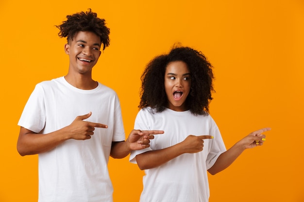 Feliz jovem bonito casal africano posando isolado sobre o espaço amarelo apontando.