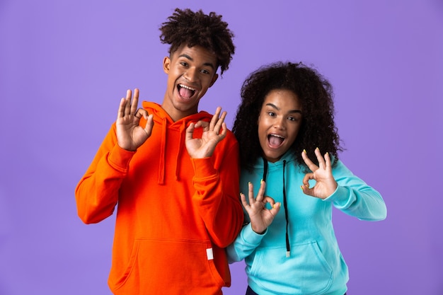 Feliz jovem bonito casal africano posando isolado sobre o espaço violeta, mostrando um gesto certo.