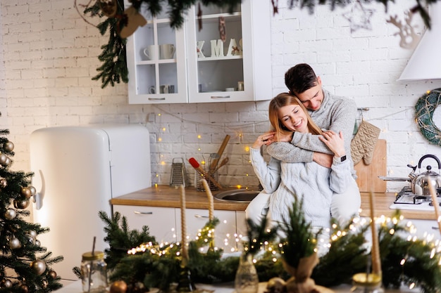 Feliz jovem casal abraçando na cozinha decorada para o ano novo interior de Ano Novo na cozinha cozinha de Natal