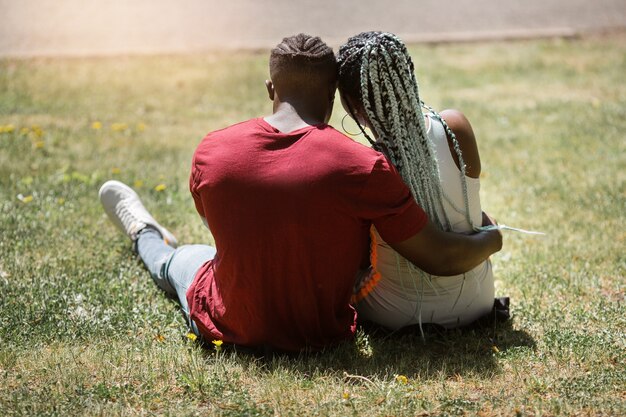 Feliz jovem casal africano de pessoas sentadas em um parque de verão na grama