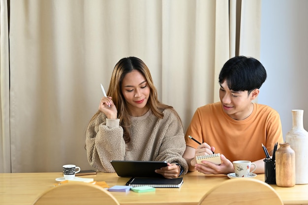 Feliz jovem casal asiático sentados juntos na sala de estar brilhante e navegando na internet com tablet digital