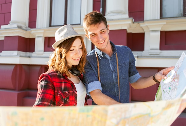 Feliz jovem casal de viajantes segurando um mapa nas mãos enquanto caminhava pela cidade. conceito de viagem